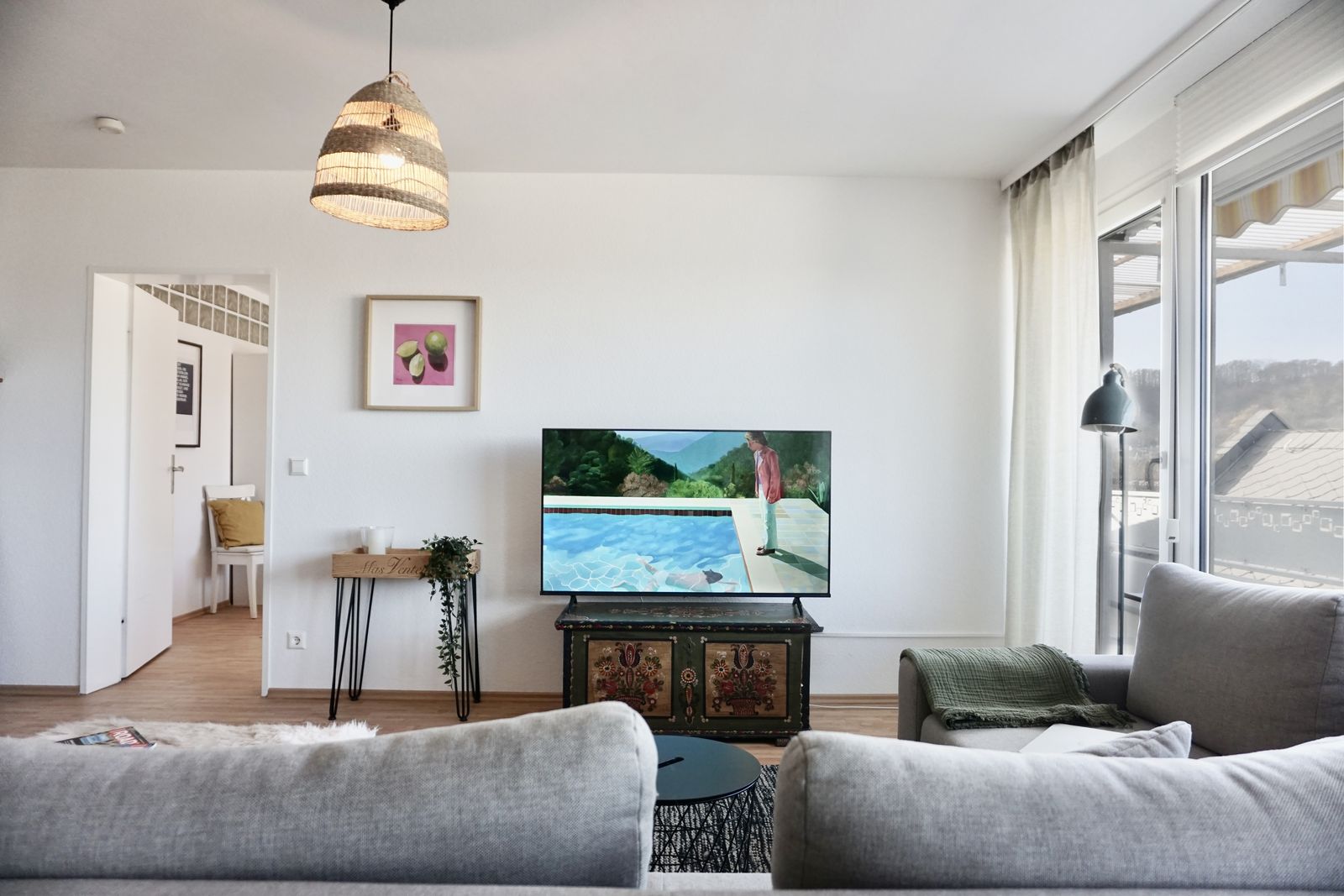 Wohnzimmer mit Sofa, Fernseher und Zugang zum Balkon